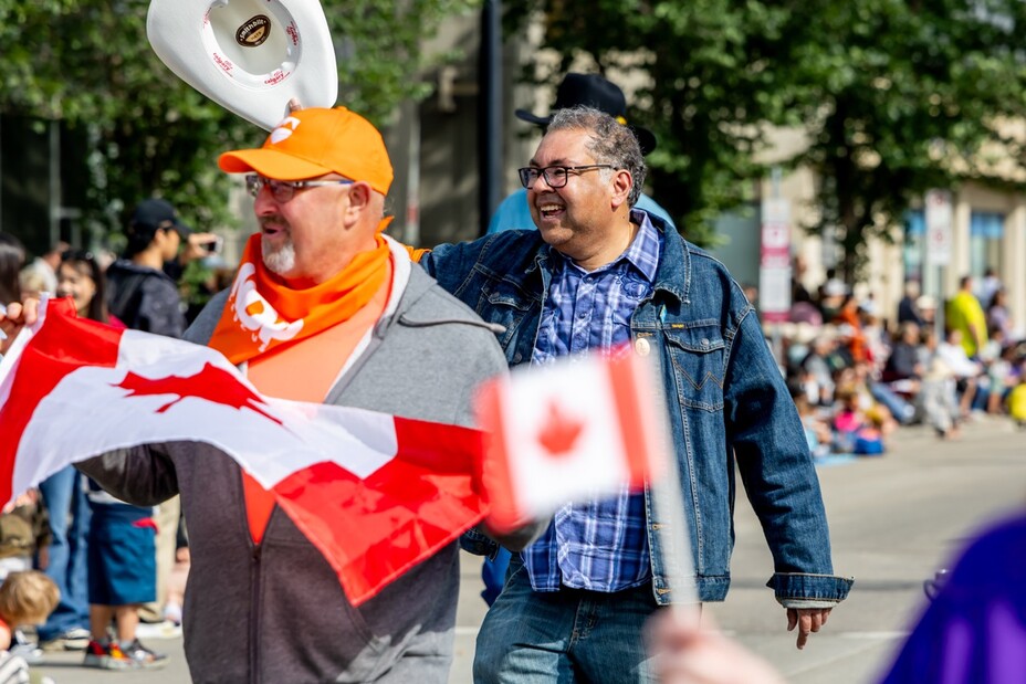 Canada Flags wave in the foreground with a supporter and Naheed Nenshi waving to parade watchers.